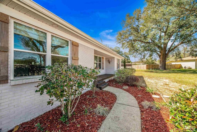 doorway to property featuring a yard, fence, and brick siding