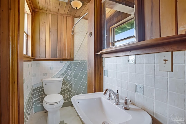 half bath with tile walls, toilet, wood ceiling, a sink, and tile patterned floors