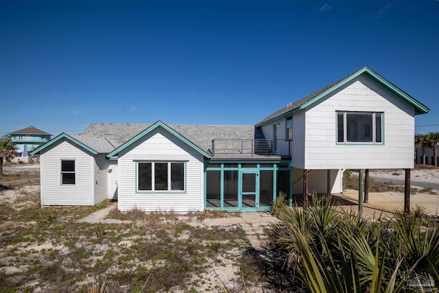 rear view of property featuring roof with shingles, a balcony, and a sunroom