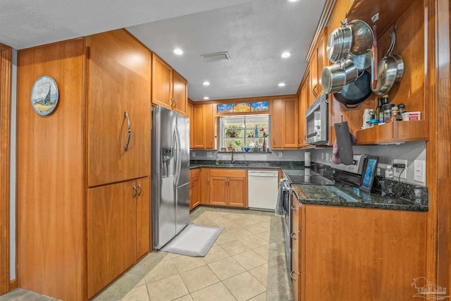 kitchen with light tile patterned floors, appliances with stainless steel finishes, sink, and dark stone countertops