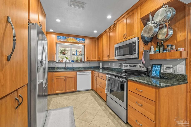 kitchen with sink, light tile patterned flooring, dark stone counters, and appliances with stainless steel finishes