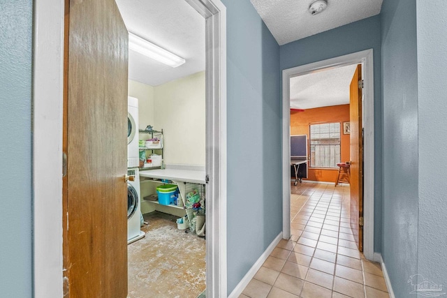 hallway with light tile patterned flooring, stacked washing maching and dryer, and a textured ceiling