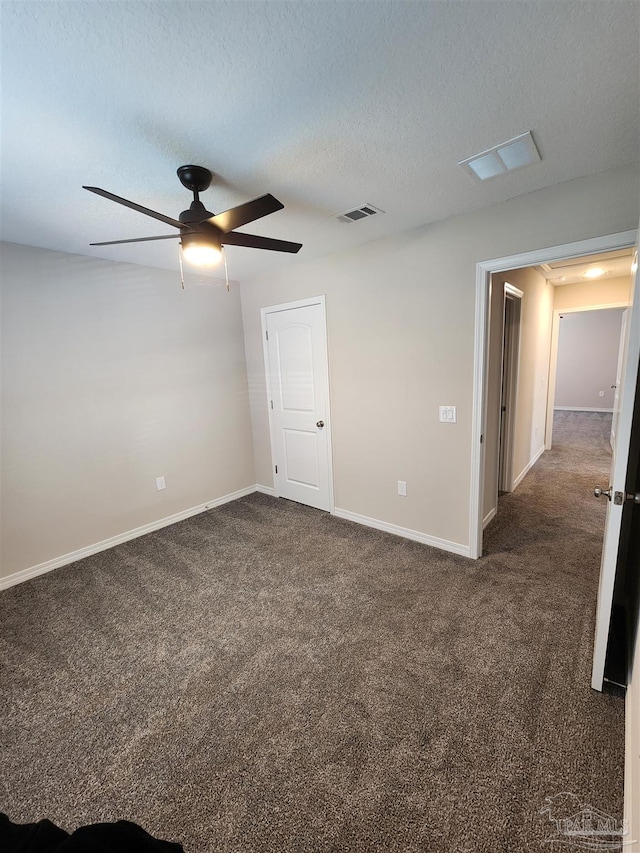 spare room featuring ceiling fan, a textured ceiling, and dark colored carpet