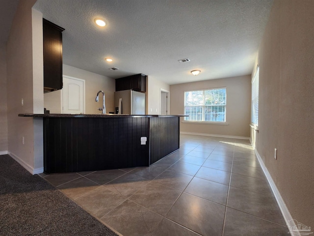 kitchen with kitchen peninsula, tile patterned floors, a textured ceiling, sink, and stainless steel fridge with ice dispenser