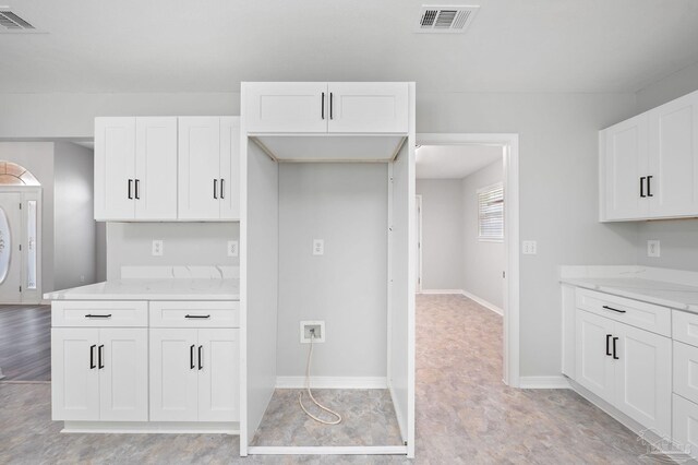 kitchen featuring baseboards, visible vents, white cabinets, and light stone counters