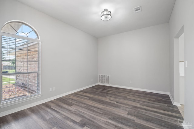 empty room featuring baseboards, visible vents, and dark wood finished floors