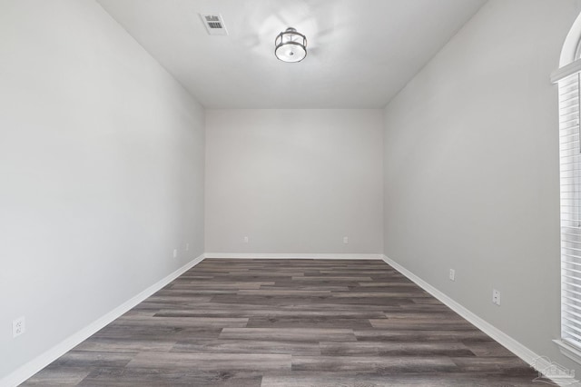 empty room featuring dark wood-type flooring, visible vents, and baseboards