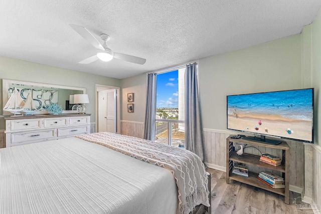 bedroom with wooden walls, light hardwood / wood-style flooring, a textured ceiling, and ceiling fan