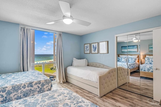 bedroom with ceiling fan, wood-type flooring, a textured ceiling, a closet, and a water view