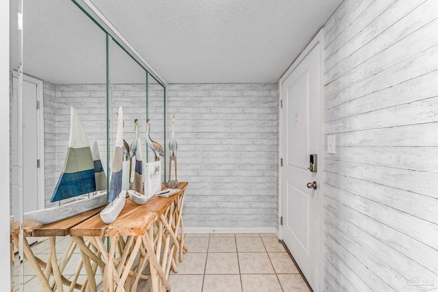 interior space featuring light tile patterned flooring, wood walls, and a textured ceiling