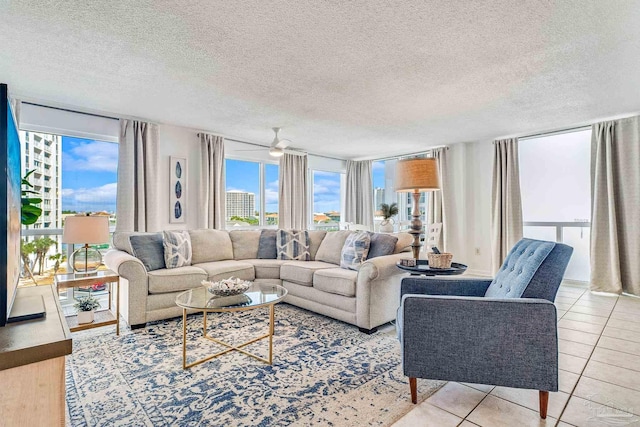 living room with ceiling fan, a wall of windows, light tile patterned floors, and a textured ceiling