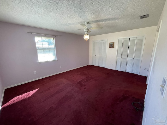 unfurnished bedroom with multiple closets, carpet flooring, a textured ceiling, and ceiling fan