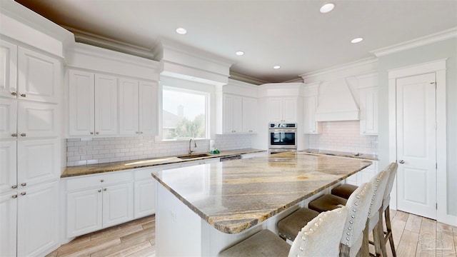 kitchen with a center island, light hardwood / wood-style floors, custom range hood, and white cabinetry