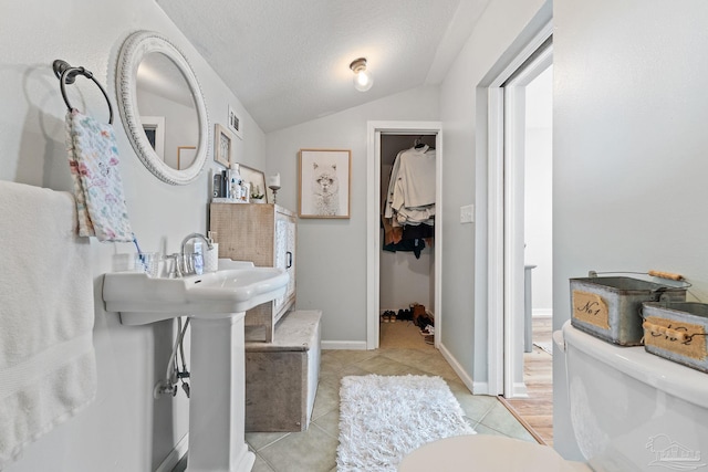 bathroom with a textured ceiling, vaulted ceiling, visible vents, and tile patterned floors