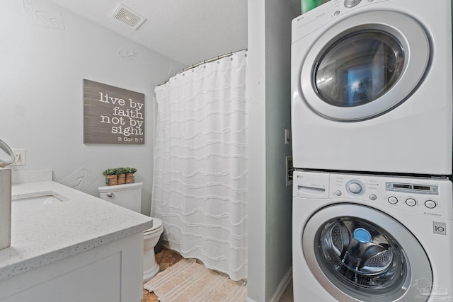 laundry area with laundry area, a textured ceiling, visible vents, and stacked washer / drying machine