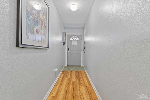 hallway featuring light wood-style flooring, baseboards, a textured ceiling, and a textured wall