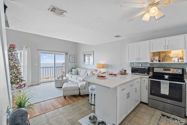 kitchen featuring a peninsula, visible vents, white cabinetry, open floor plan, and electric stove