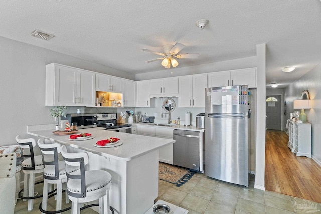 kitchen with white cabinets, appliances with stainless steel finishes, a peninsula, light countertops, and a sink