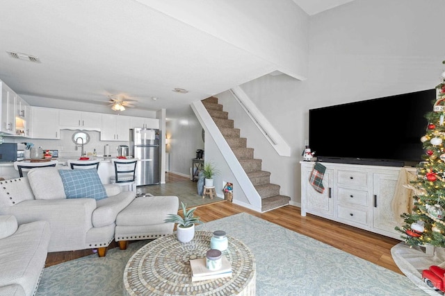 living room featuring a ceiling fan, visible vents, stairs, baseboards, and light wood-type flooring