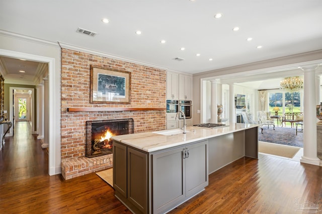 kitchen with sink, light stone countertops, an island with sink, and ornate columns