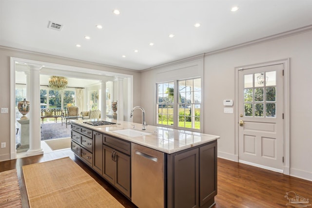 kitchen featuring sink, appliances with stainless steel finishes, decorative columns, ornamental molding, and a center island with sink