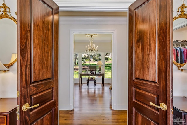 hallway featuring a notable chandelier, wood-type flooring, and ornamental molding