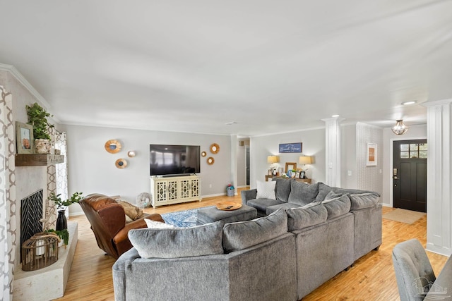 living room with light wood finished floors, baseboards, ornamental molding, a fireplace, and ornate columns