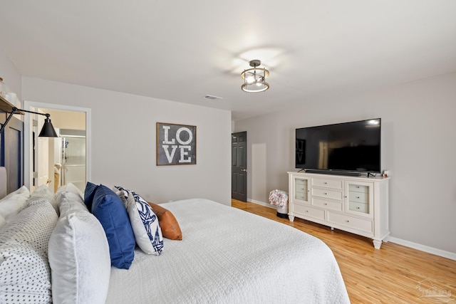 bedroom featuring visible vents, baseboards, ensuite bath, and wood finished floors