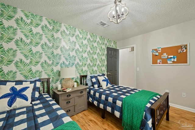 bedroom with a textured ceiling, light wood-style floors, baseboards, and a chandelier