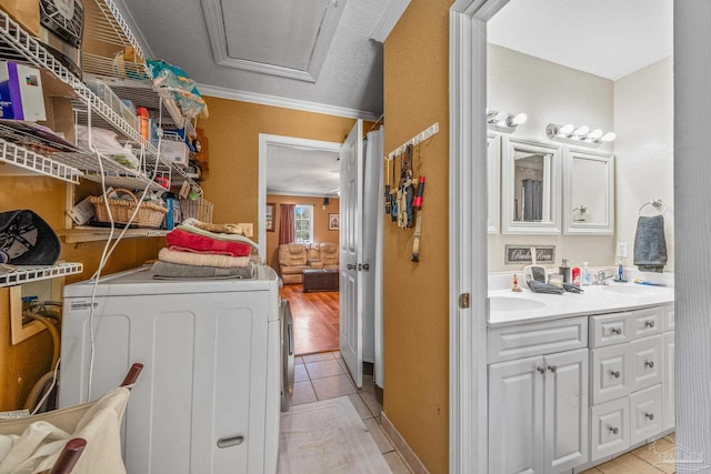 washroom with light tile patterned floors, washing machine and dryer, laundry area, a sink, and ornamental molding