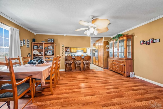 dining space featuring ornamental molding, baseboards, a textured ceiling, and light wood finished floors