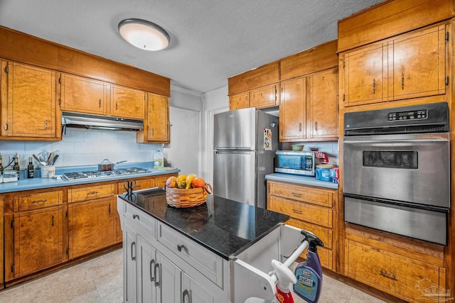 kitchen with under cabinet range hood, appliances with stainless steel finishes, brown cabinets, and a warming drawer