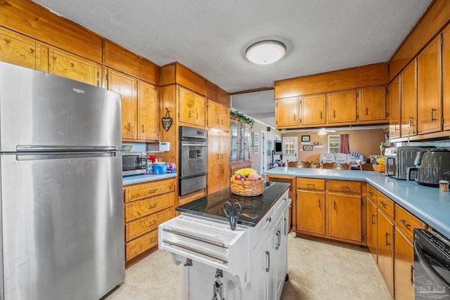 kitchen featuring appliances with stainless steel finishes, brown cabinets, light countertops, a textured ceiling, and a warming drawer