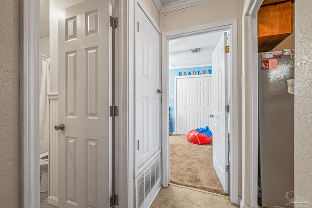 corridor with light carpet, visible vents, and a textured wall