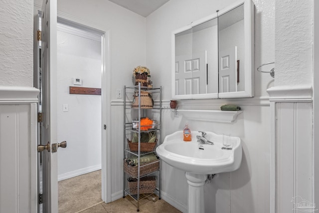 bathroom featuring a wainscoted wall, tile patterned floors, and a decorative wall