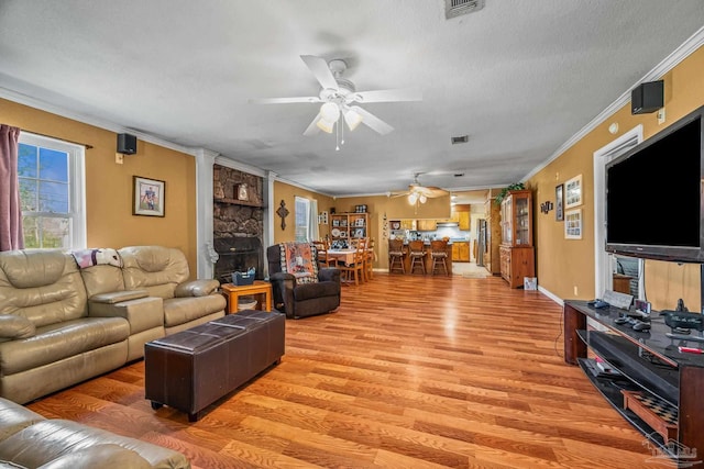 living area with a textured ceiling, light wood-style flooring, visible vents, a ceiling fan, and ornamental molding