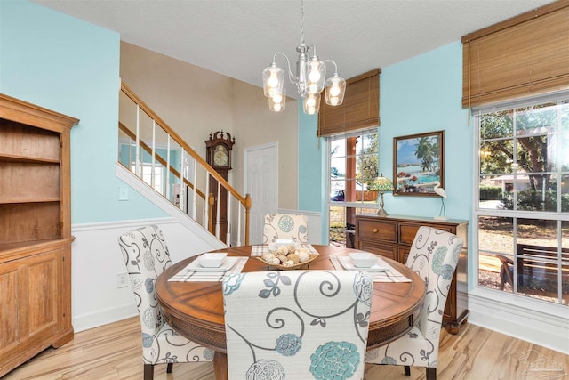 dining room with light wood-type flooring, stairs, a textured ceiling, and a notable chandelier