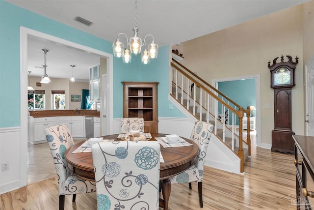 dining room with visible vents, an inviting chandelier, wainscoting, light wood-type flooring, and stairs