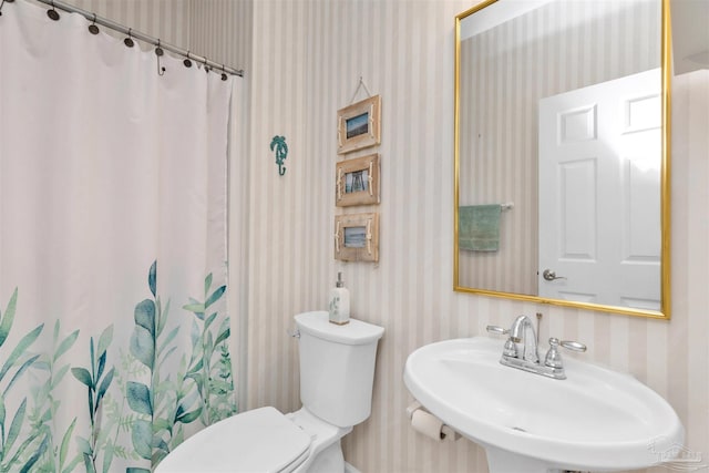 bathroom with toilet, wallpapered walls, a sink, and a shower with shower curtain