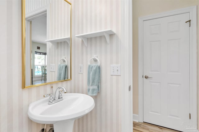 bathroom with wood finished floors, a sink, and wallpapered walls