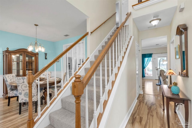 staircase featuring visible vents, a notable chandelier, baseboards, and wood finished floors