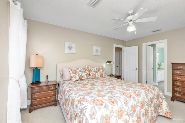 carpeted bedroom featuring a textured ceiling, ensuite bathroom, visible vents, and a ceiling fan