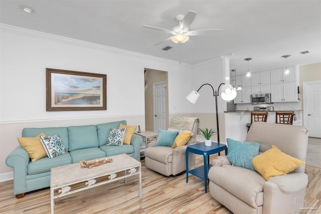 living room featuring light wood-style flooring, a ceiling fan, visible vents, and crown molding