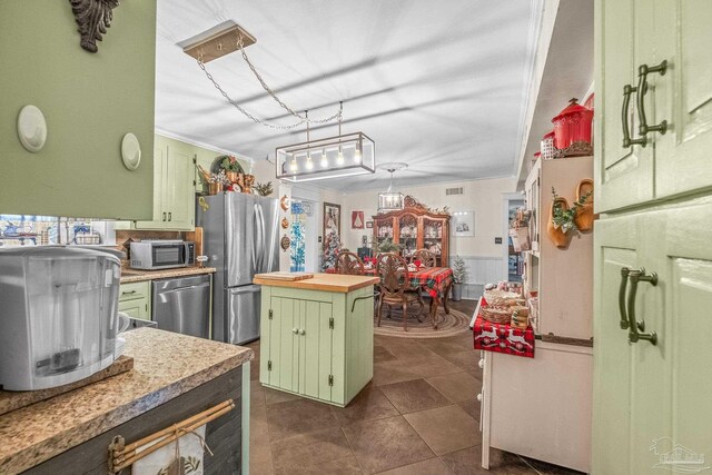 kitchen with dark tile patterned flooring, green cabinets, ornamental molding, and stainless steel appliances