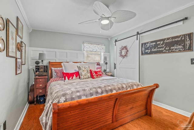 bedroom with a barn door, ceiling fan, crown molding, and hardwood / wood-style flooring