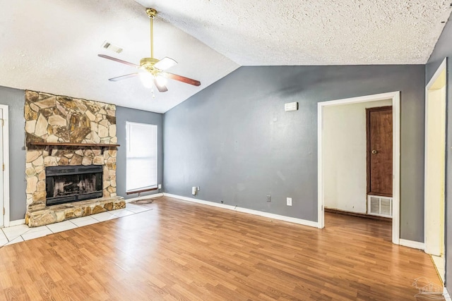 unfurnished living room with a stone fireplace, vaulted ceiling, ceiling fan, light wood-type flooring, and a textured ceiling