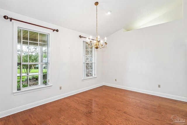 spare room with a notable chandelier, hardwood / wood-style flooring, and vaulted ceiling