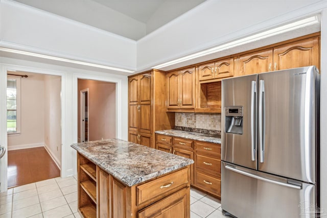 kitchen with a center island, decorative backsplash, light tile patterned floors, light stone countertops, and stainless steel fridge