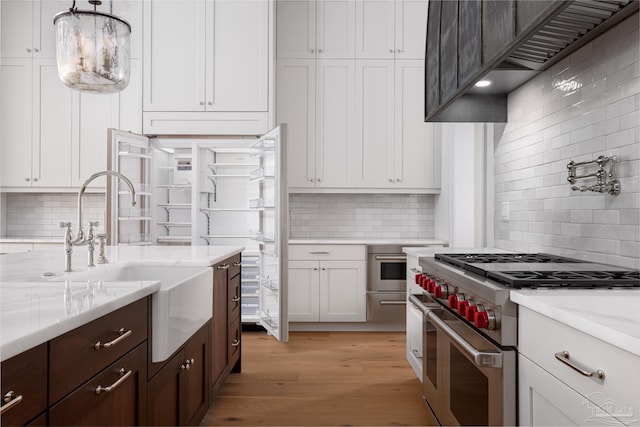 kitchen featuring dark brown cabinetry, stainless steel appliances, a sink, light wood-style floors, and white cabinets