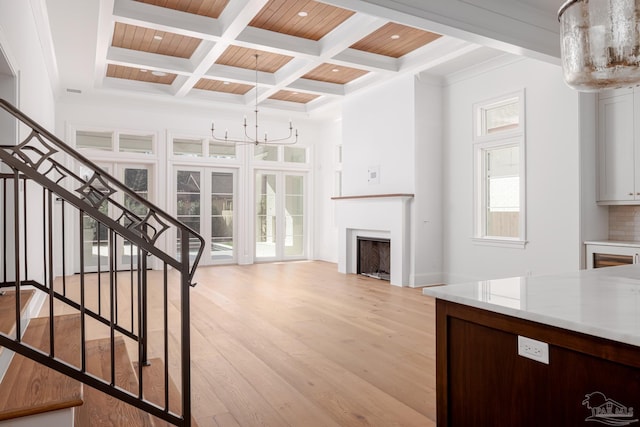 unfurnished living room featuring a fireplace, light wood-style floors, coffered ceiling, beamed ceiling, and stairs